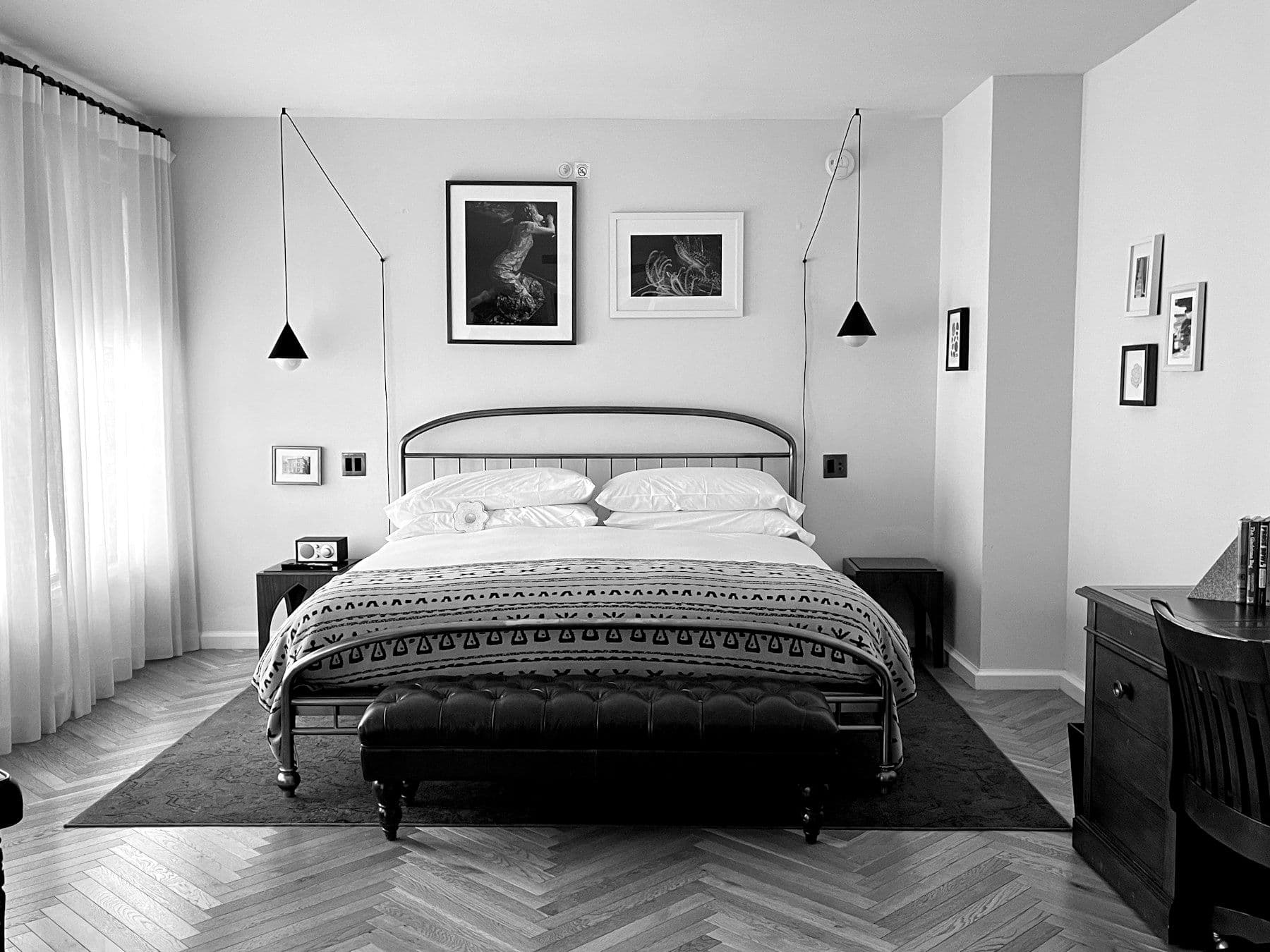 A bright guest room with a metal bed and framed photographs